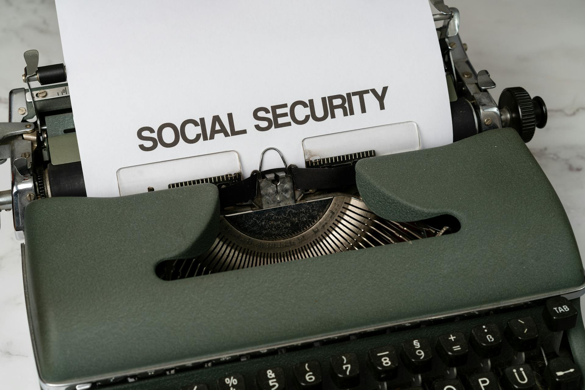 A typewriter with a sheet of paper showing the words "SOCIAL SECURITY" typed in bold uppercase letters.