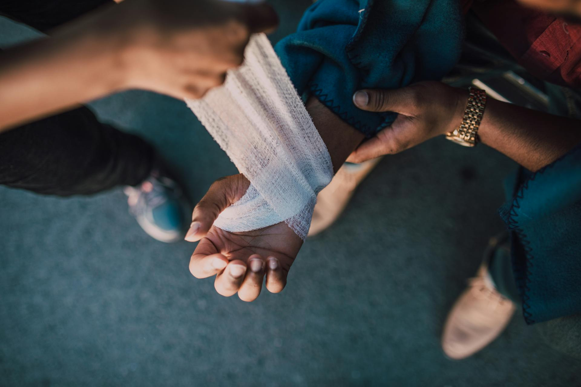 A person wraps another person’s wrist with a white bandage while they are seated, as seen from above.