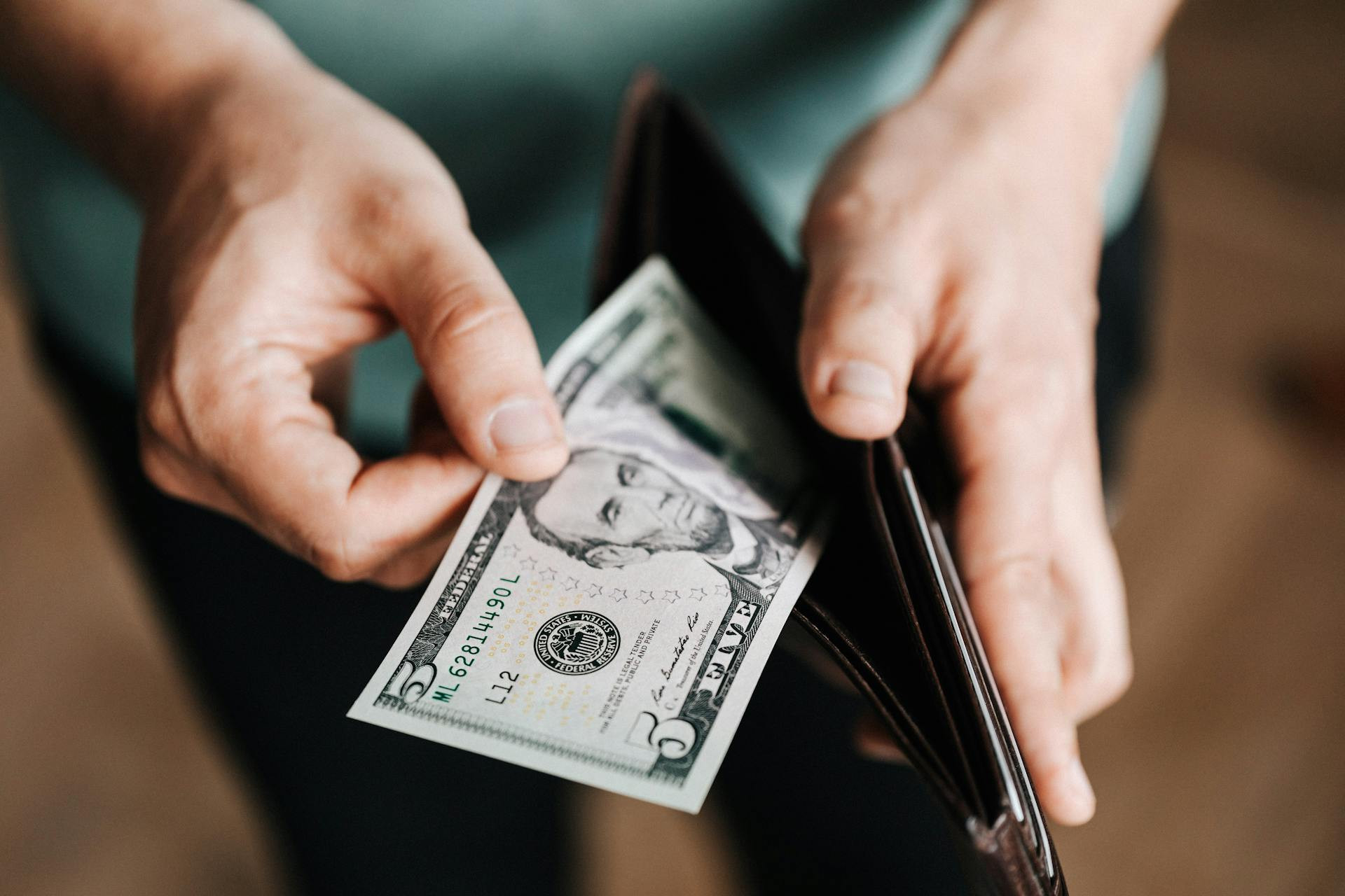 A person holding a wallet and taking out a five-dollar bill.