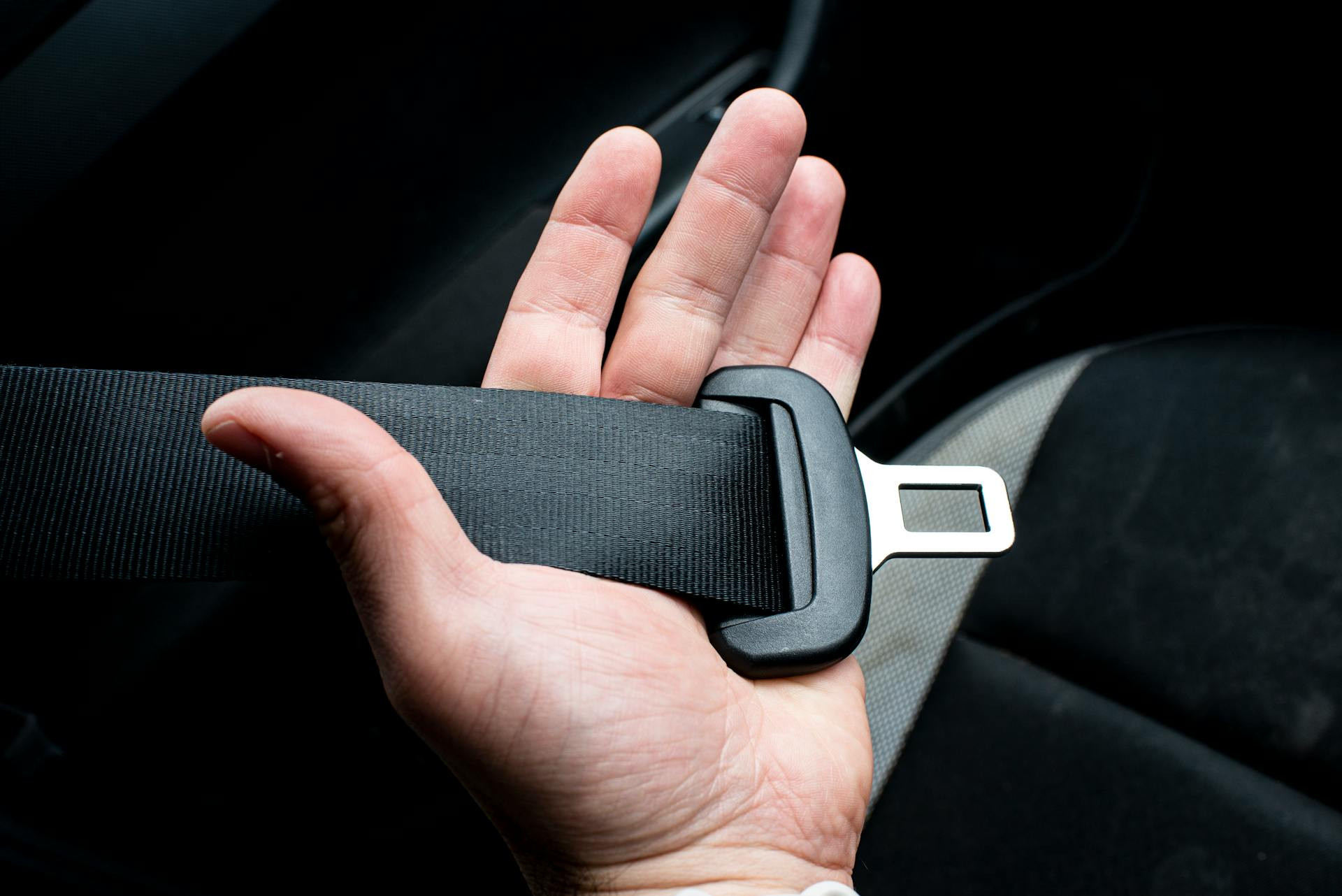 A person holds a car seat belt and buckle in their hand, positioned inside a vehicle.