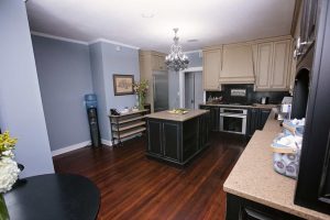 Modern kitchen with dark wood floors, beige cabinets, a central island, stainless steel appliances, and a chandelier; decorative items and a water cooler are also visible.