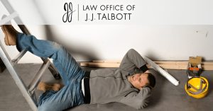 A man lies on the floor next to a ladder, appearing to have fallen, with construction materials and a hard hat nearby; "Law Office of J.J. Talbott" logo is above.