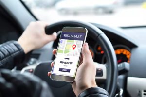 Person holding a smartphone with a rideshare app displaying a new ride request while driving a car.