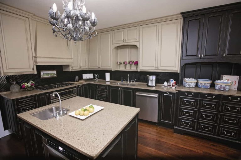 Modern kitchen with cream and dark wood cabinets, granite countertops, a central island with a sink, stainless steel appliances, and a decorative chandelier.