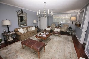 A traditional living room with a brown sofa, armchairs, a large rug, a chandelier, and neutral decor in a soft gray color scheme.