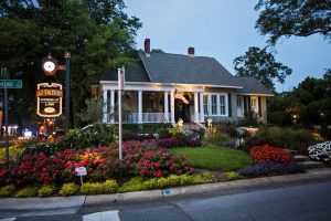 A small law office in a white historic house with a wraparound porch, surrounded by colorful flower beds and greenery at dusk.