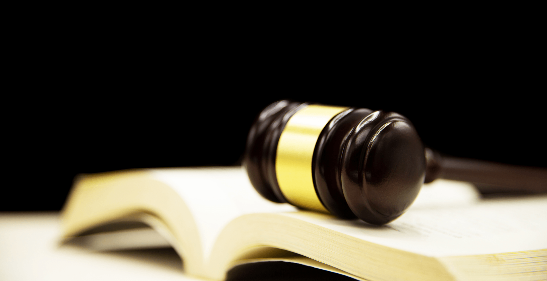 A wooden judge’s gavel rests on top of an open book against a black background.