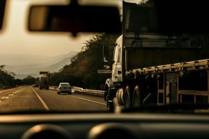View from inside a car driving on a highway, with a truck passing on the right and other vehicles ahead, mountains visible in the background.