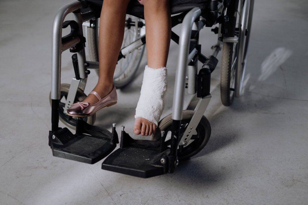 A person sitting in a wheelchair with one leg in a cast and the other foot in a pink shoe.