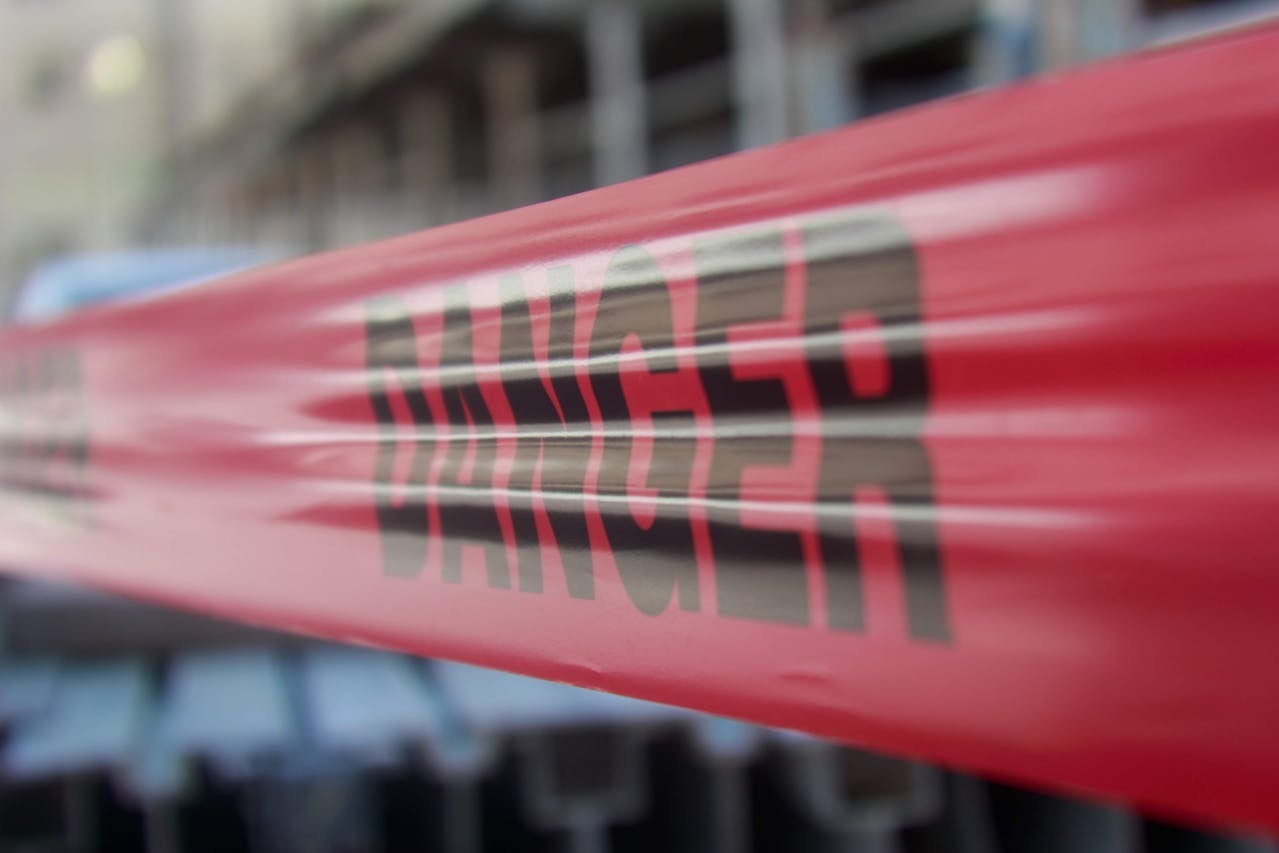 Close-up of red caution tape with the word "DANGER" printed on it, stretched across a blurred background of a construction site.