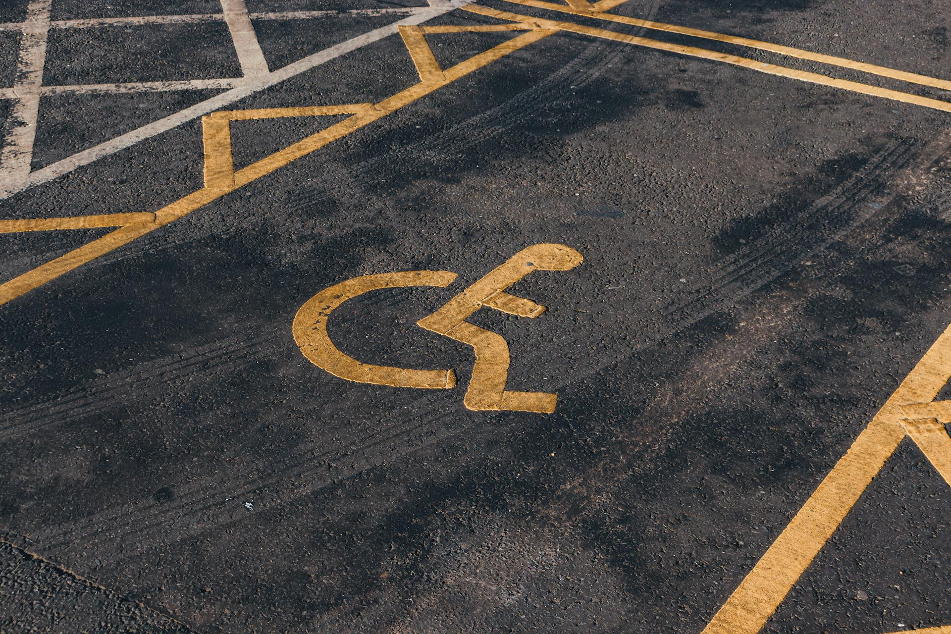 Close-up of a yellow wheelchair symbol painted on asphalt, marking a designated accessible parking space with distinct yellow lines.