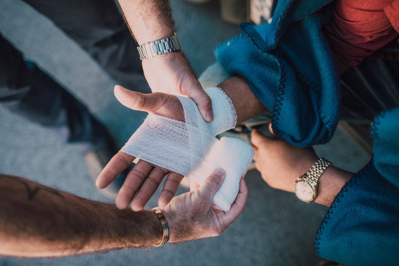 A person wraps a bandage around another person’s injured hand while both are seated.