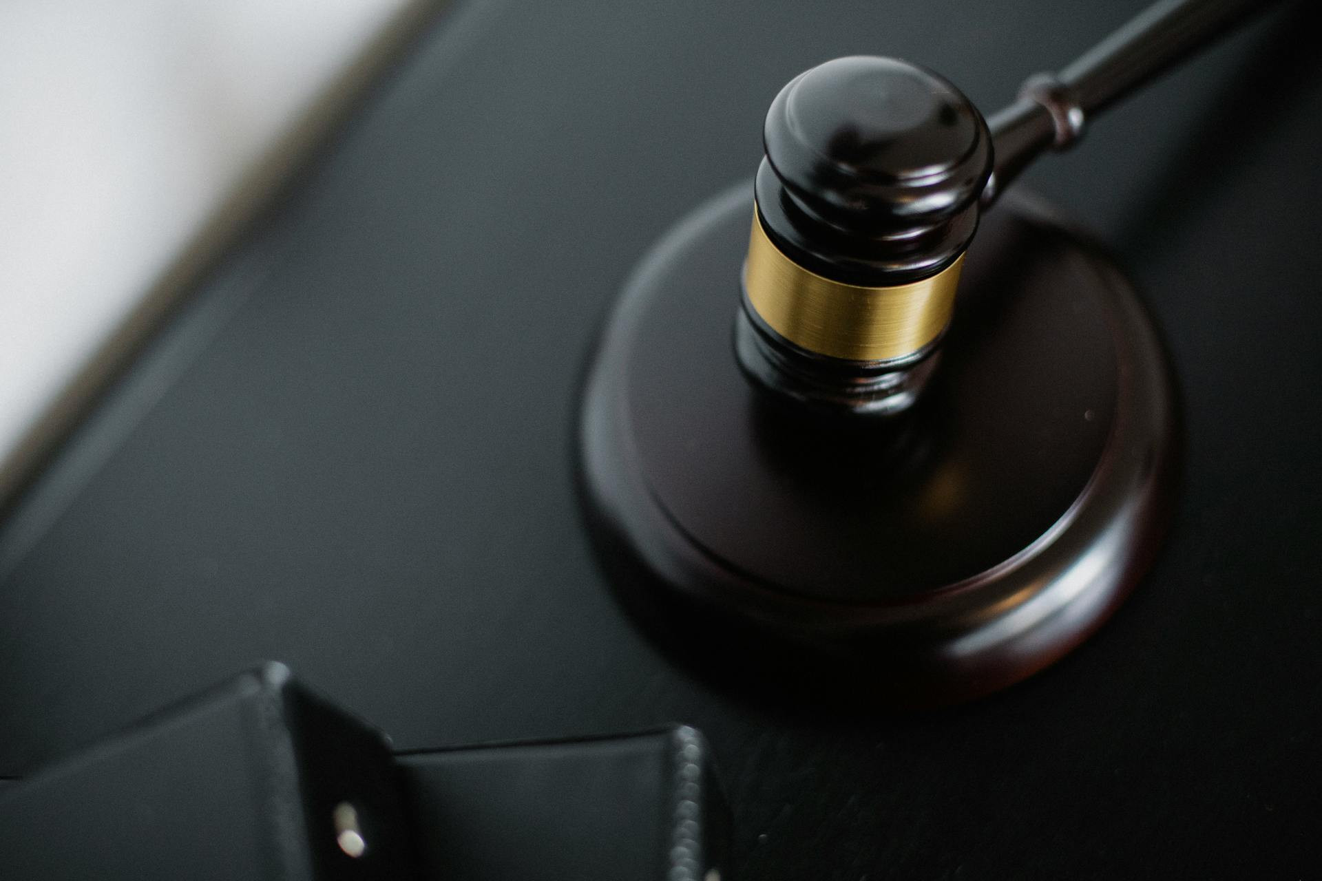A close-up view of a wooden judge's gavel resting on a sound block, with part of a black wallet nearby on a dark surface.