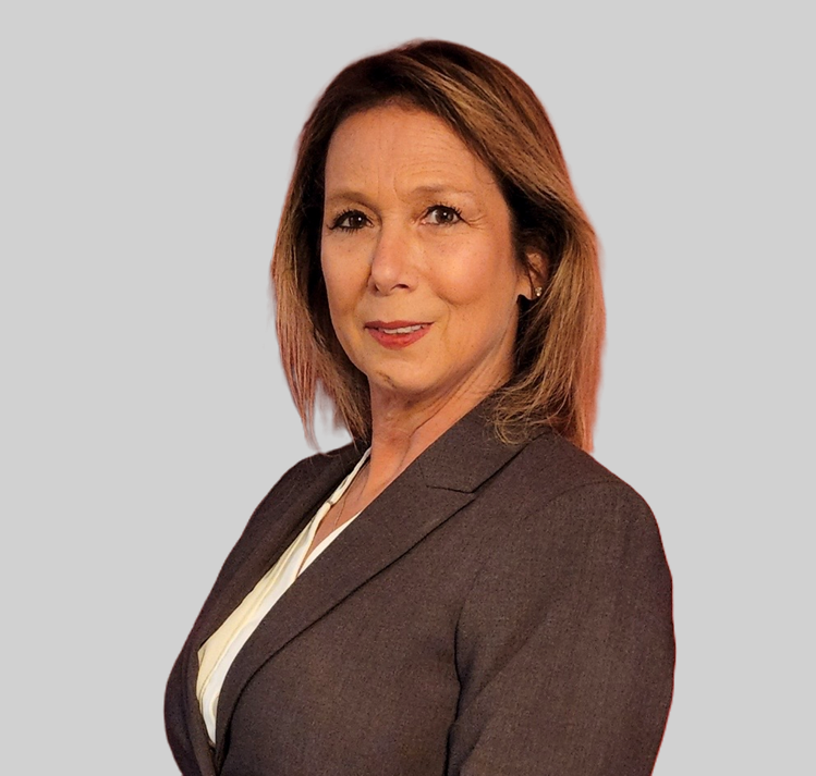 A woman with shoulder-length light brown hair wearing a gray blazer and white top poses against a plain light gray background.